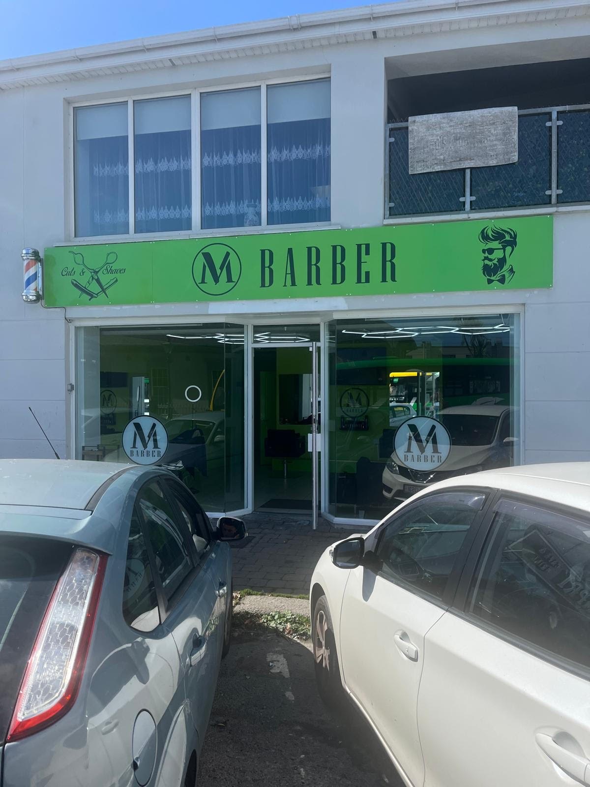 The M Barber shopfront at Station House, 2 Florence Road, Bray — lime-green BARBER sign, circled M logo in the windows, and the pole over the door